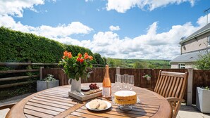 A round wooden table with a cake, a bottle, and a plate of cookies. - Bwthyn-Bwlch -  a self catering cottage that sleeps 4 guests in 2 bedrooms (Dinbych)