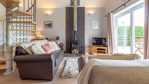 A modern living room with a fireplace, a sofa, a TV, and a spiral staircase. - Bwthyn-Bwlch -  a self catering cottage that sleeps 4 guests in 2 bedrooms (Dinbych)