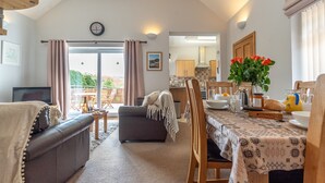 A living room with a sofa, a dining table with chairs, a kitchen area, and a balcony with curtains. - Bwthyn-Bwlch -  a self catering cottage that sleeps 4 guests in 2 bedrooms (Dinbych)