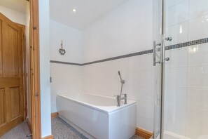 Et badeværelse med et hvidt badekar, en bruseniche og en trædør.