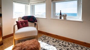 Een kamer met een stoel, een vloerkleed, een raam met uitzicht en een flesje op de vensterbank.