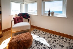 Ein Zimmer mit Stuhl, Teppich, Fenster und Blick sowie einer Flasche auf der Fensterbank.