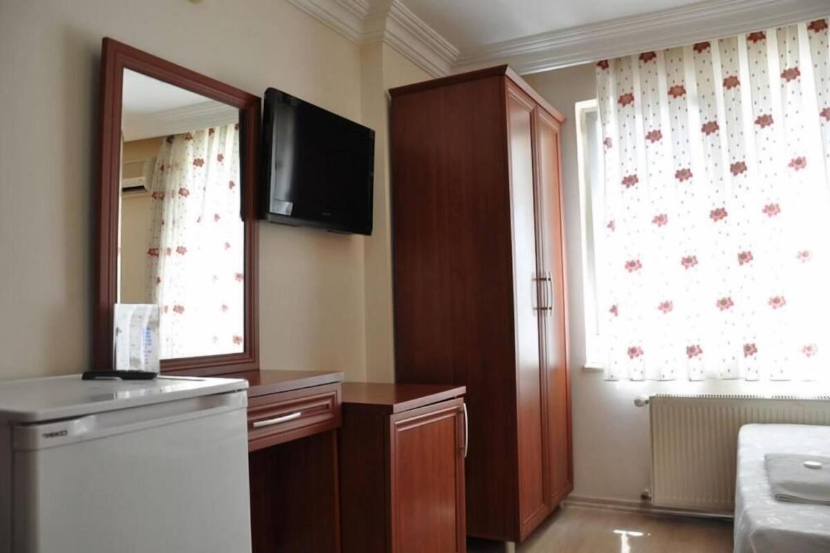 Une chambre avec un lit, une armoire, une télévision et une fenêtre avec des rideaux.