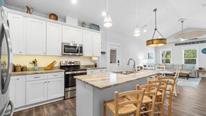 Une cuisine moderne avec des meubles blancs, des appareils en acier inoxydable et un îlot central doté de tabourets de bar.