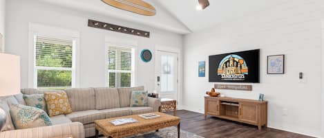 A spacious living room with a large sofa, a coffee table, and a television mounted on the wall.