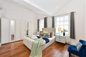 Ein Schlafzimmer mit Bett, Nachttisch, Lampe, Vorhängen und einem Kleiderschrank.