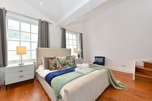 Ein Schlafzimmer mit Bett, Nachttisch, Lampe und Blick ins Freie durch große Fenster.