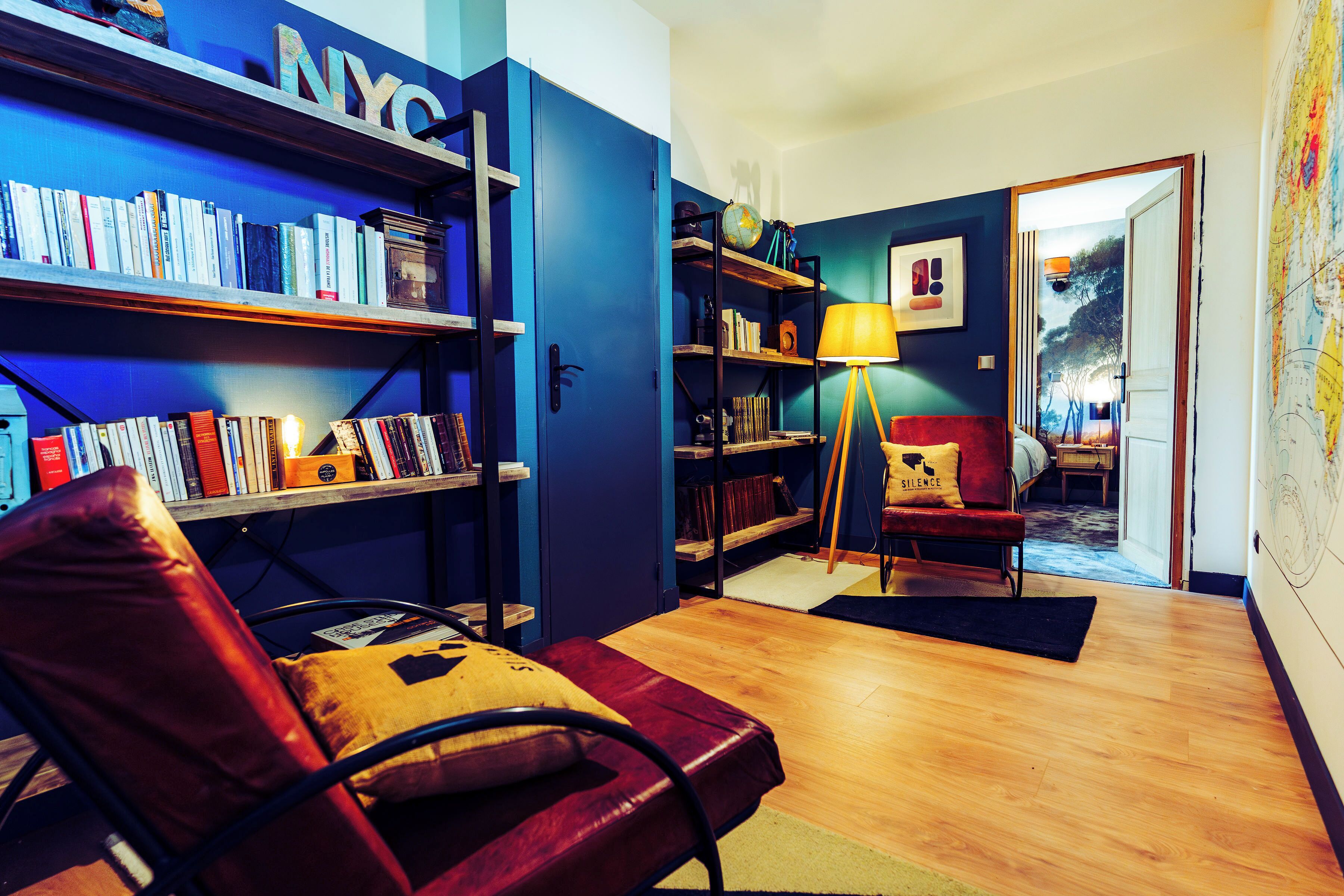 Une pièce comprenant une bibliothèque, un fauteuil en cuir, une lampe et une porte donnant sur une autre pièce.