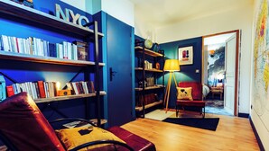 Um quarto com estante de livros, poltrona de couro, luminária e porta que dá para outro aposento.