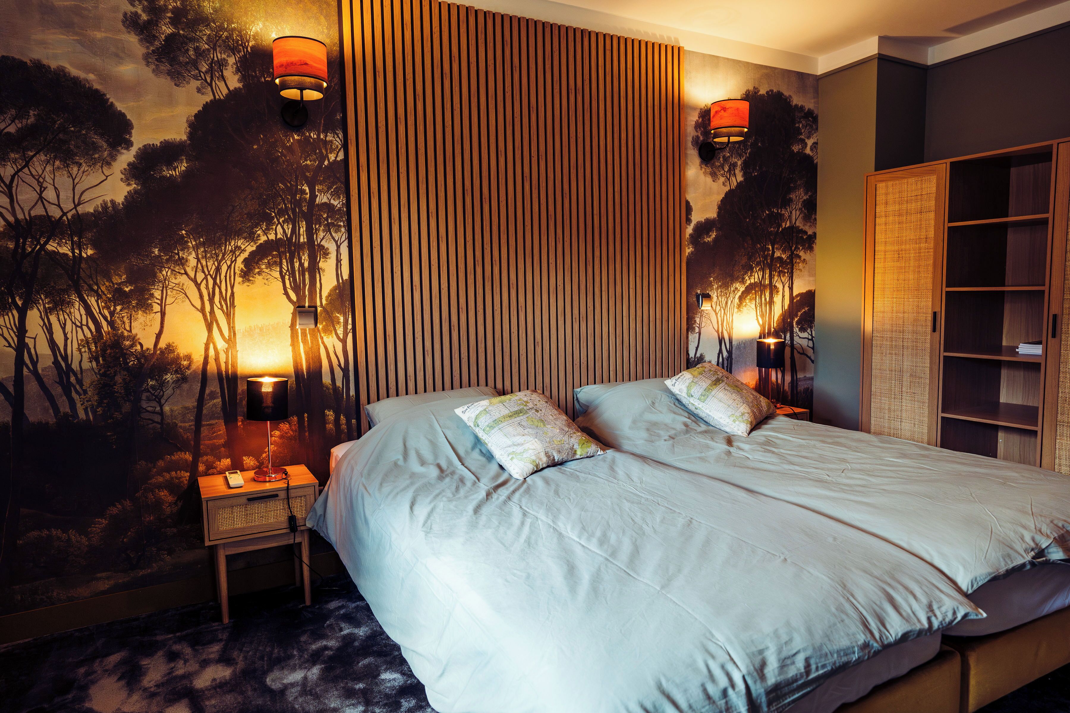 Un lit double avec deux oreillers, une table de chevet avec une lampe, une étagère fixée au mur et une armoire.