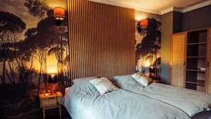 Uma cama de casal com duas almofadas, uma mesa de cabeceira com abajur, uma estante na parede e um guarda-roupa.
