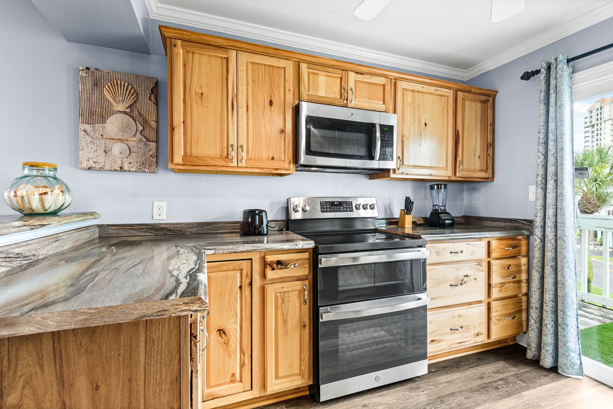 A kitchen with wooden cabinets, a stainless steel oven, a microwave, and a marble countertop.