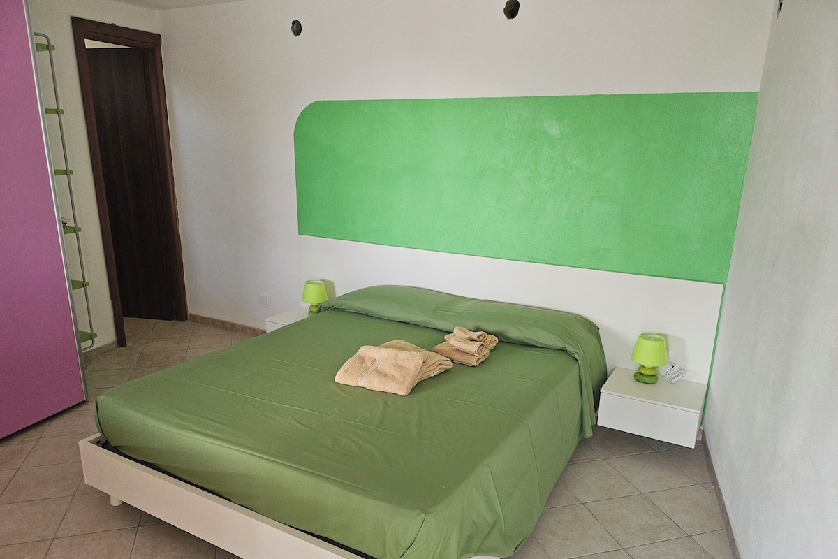 A room with a bed, green headboard, two bedside tables with lamps, and a door.