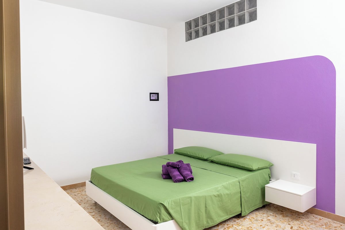 A bedroom with a white bed, green bedding, and a purple accent wall.