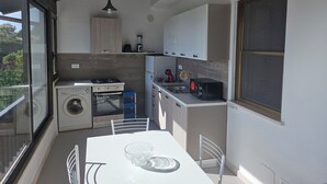 A compact kitchen with a washing machine, a stove, a microwave, and a dining area with a table and chairs. - Lilium Gaeta Apartment by Mamo Florence (Gaeta)