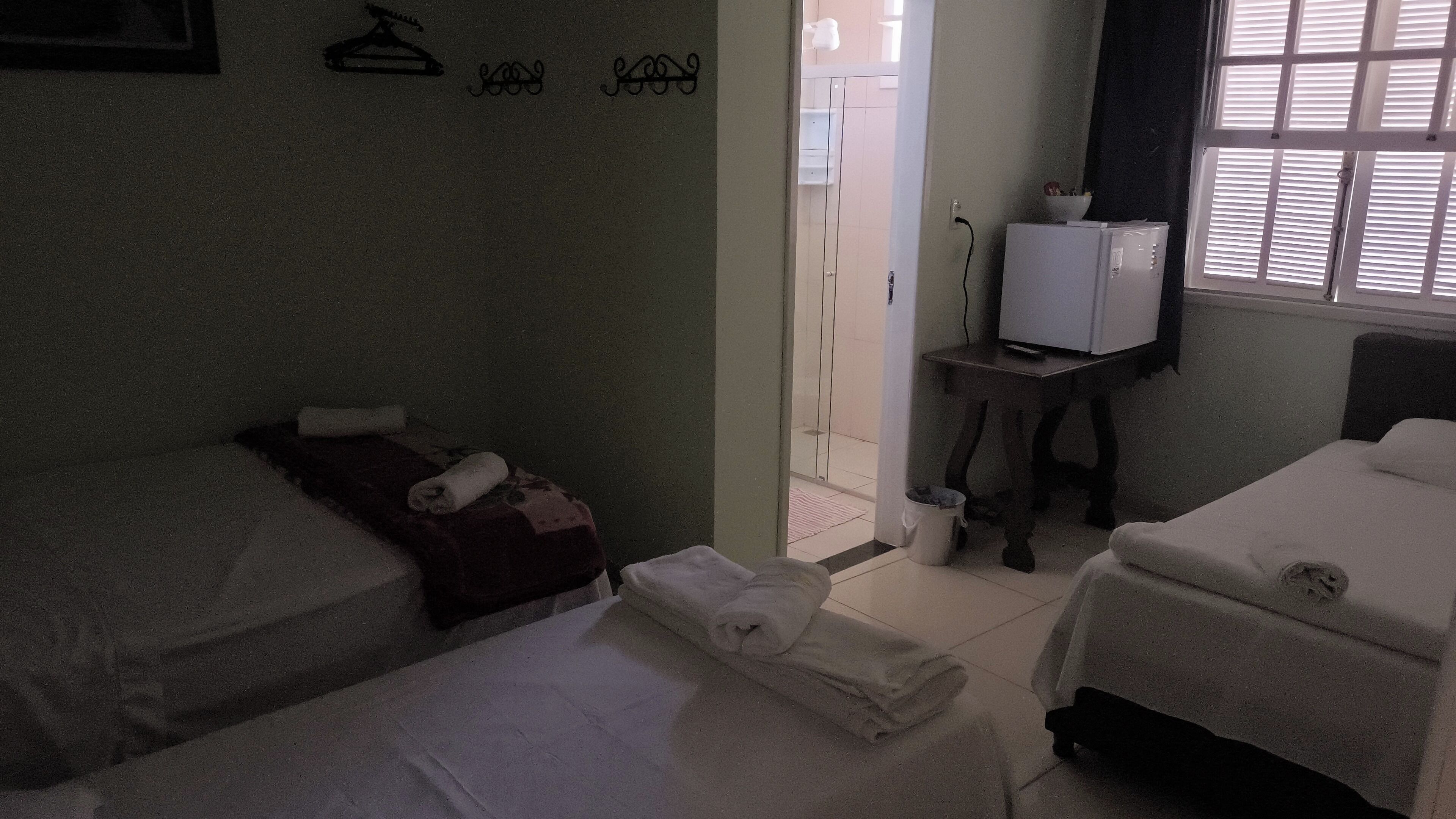 A hotel room with two beds, a small table with a TV, and a window with blinds.