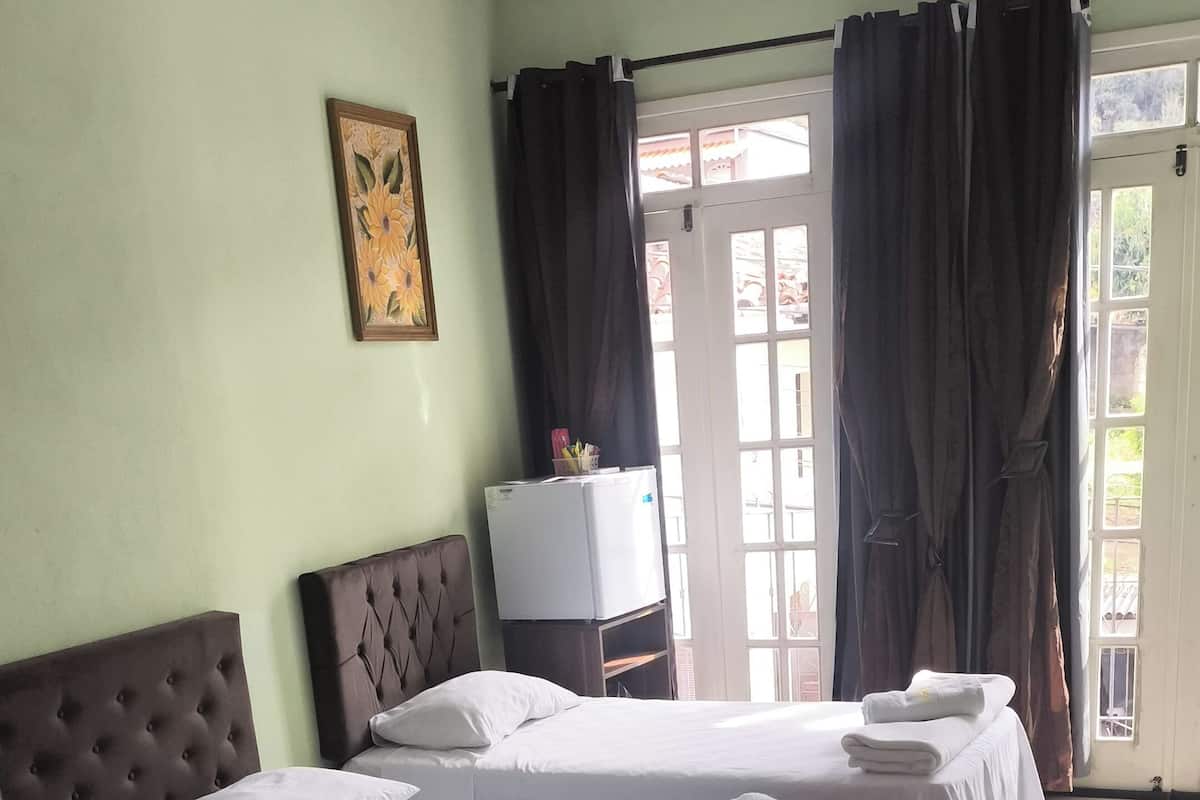 Una habitación de hotel con tres camas, televisión y ventana con cortinas.