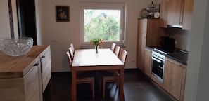 Una cocina compacta con armarios de madera, una mesa de comedor con sillas, un jarrón con flores y una ventana con vistas a zonas verdes.