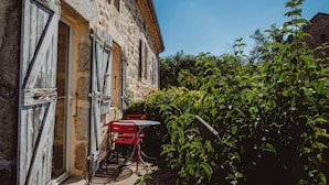 A rustic stone building with a wooden door and shuttered windows, a small outdoor table and chairs, and lush green foliage. - Ardèche estate from 1748 - Private heated pool - 16 travelers (Saint-Barthélemy-Grozon)