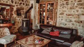 A rustic room with a stone wall, a large wood-burning stove, a leather sofa, a wooden coffee table, and a checkered chair. - Ardèche estate from 1748 - Private heated pool - 16 travelers (Saint-Barthélemy-Grozon)
