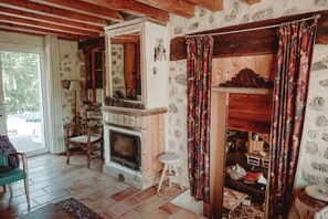 Ein rustikaler Innenraum mit Kamin, Steinwänden, Holzbalken und einer gemütlichen Sitzecke.