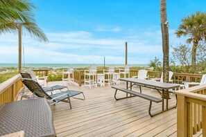 A wooden deck with outdoor seating, including chairs and a table, overlooking a beach.