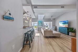 A modern living room with a sofa, a TV, and a kitchen area with stools.