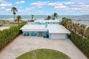 A two-story building with a flat roof, a covered patio area with blue chairs, and a view of the ocean.