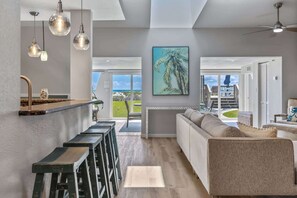 A modern kitchen with pendant lights, a dining area with a sofa, and a view through large glass doors.