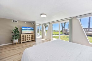 A bedroom with a large bed, a TV on a wooden cabinet, and a view of the outdoors.