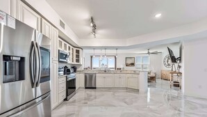 Eine geräumige Küche mit Edelstahl-Kühlschrank, Mikrowelle und Geschirrspüler, einer großen Kochinsel mit Spüle und einem Deckenventilator.