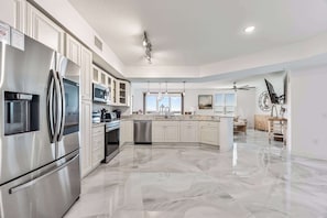 A spacious kitchen with a stainless steel refrigerator, microwave, and dishwasher, a large island with a sink, and a ceiling fan. - River Fly-In | Luxury Launch View Retreat (Merritt Island)