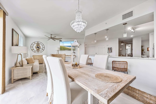 A spacious dining area with a wooden table, white upholstered chairs, a chandelier, and a ceiling fan. - River Fly-In | Luxury Launch View Retreat (Merritt Island)