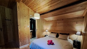 A wooden room with a bed, bedside lamps, and a hanging light fixture.
