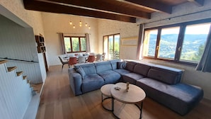 A spacious living area with a large sectional sofa, a round coffee table, and a dining area with a table and chairs.