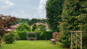 Ein grüner Hinterhof mit einer Holz-Pergola, einer Schaukel und einer Steinsitzbank.