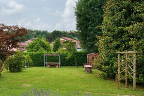 Ein grüner Hinterhof mit einer Holz-Pergola, einer Schaukel und einer Steinsitzbank.