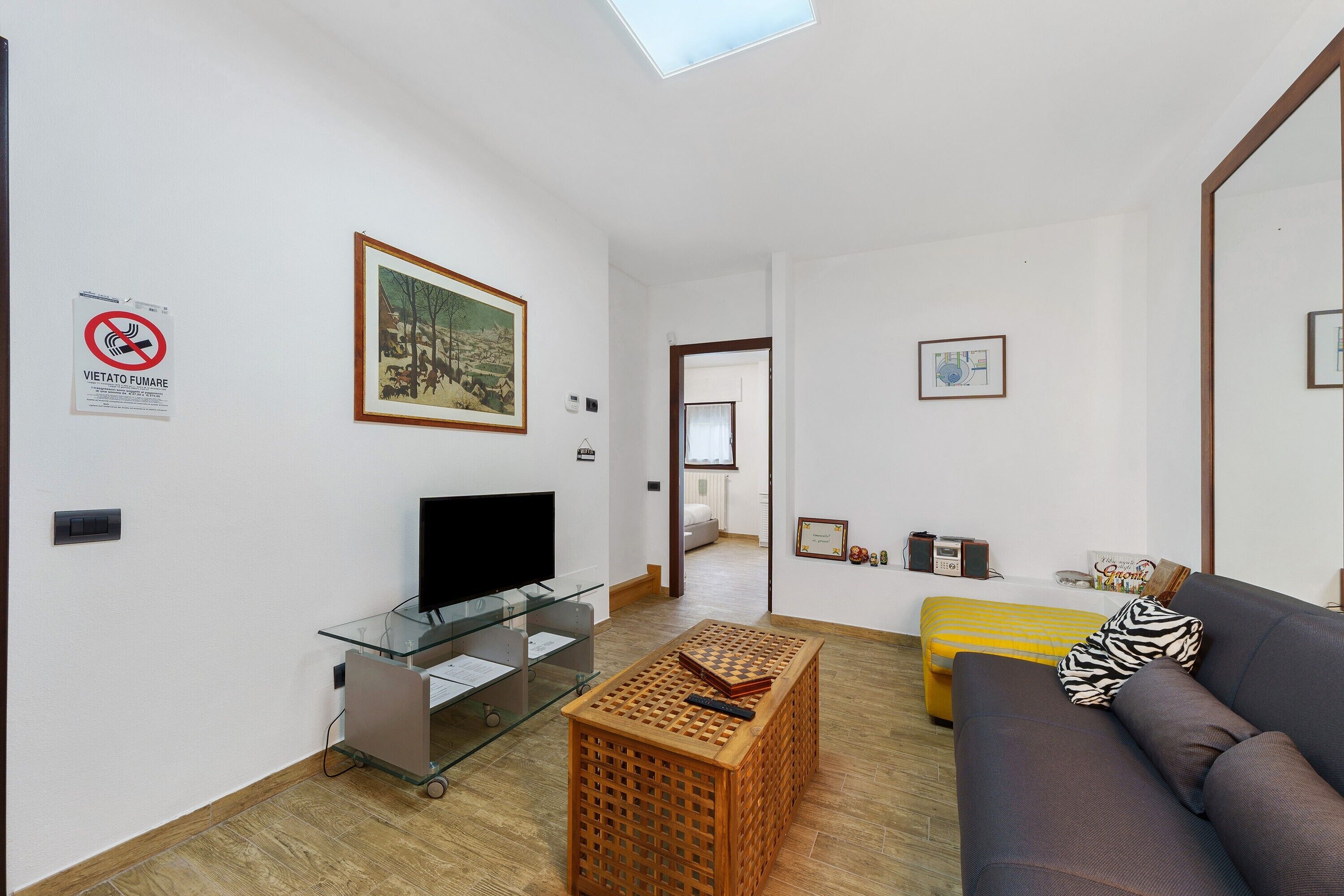Ein Wohnzimmer mit Fernseher, einer Glasschrank, einer Holzkiste, einem Sofa und einem gelben Ottoman.