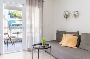 Una sala de estar moderna con un sofá gris, una mesita redonda con una planta, y un balcón con mesa y sillas.