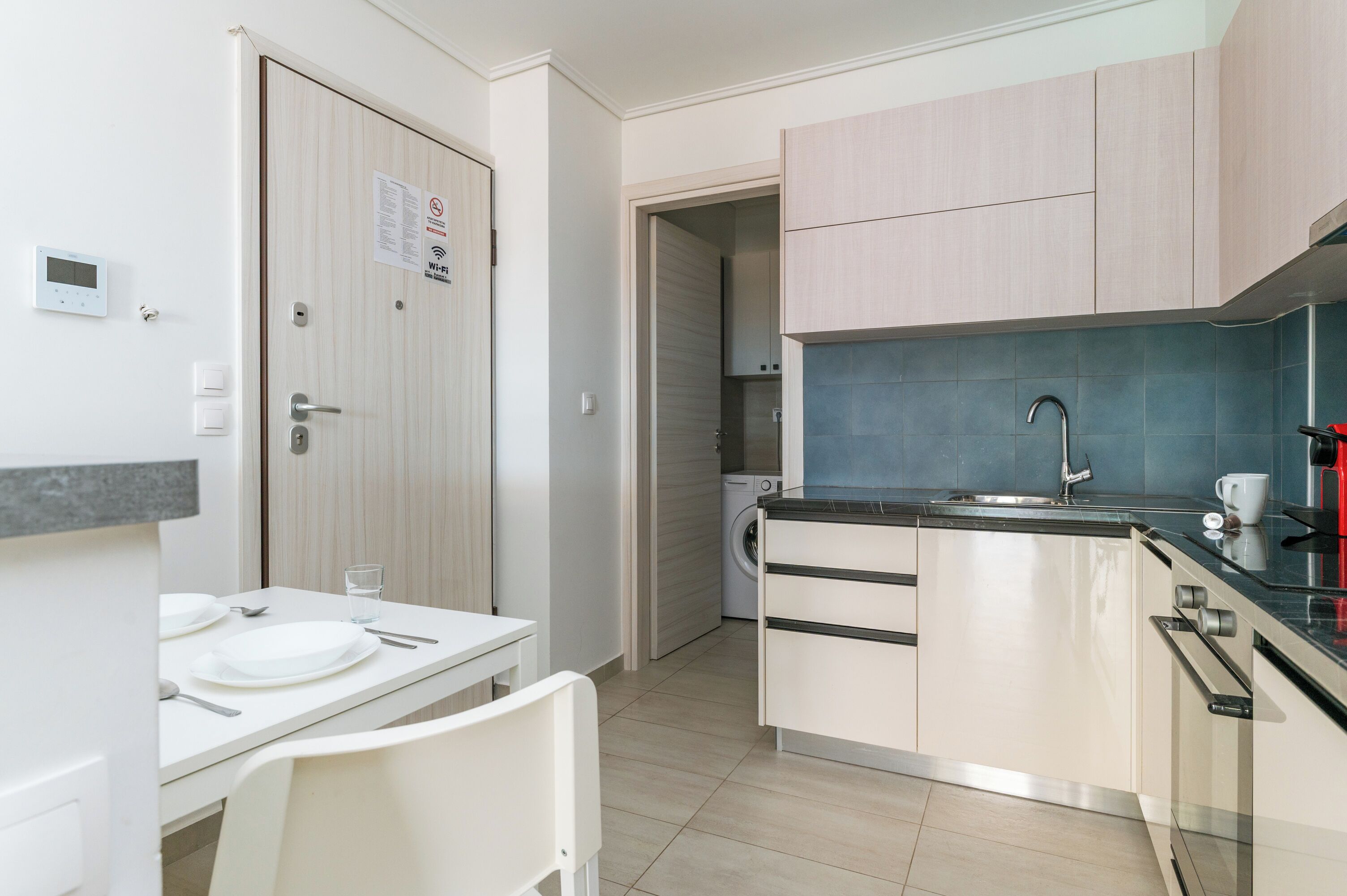 A compact kitchen with a sink, a washing machine, and a dining area with a table and chairs.