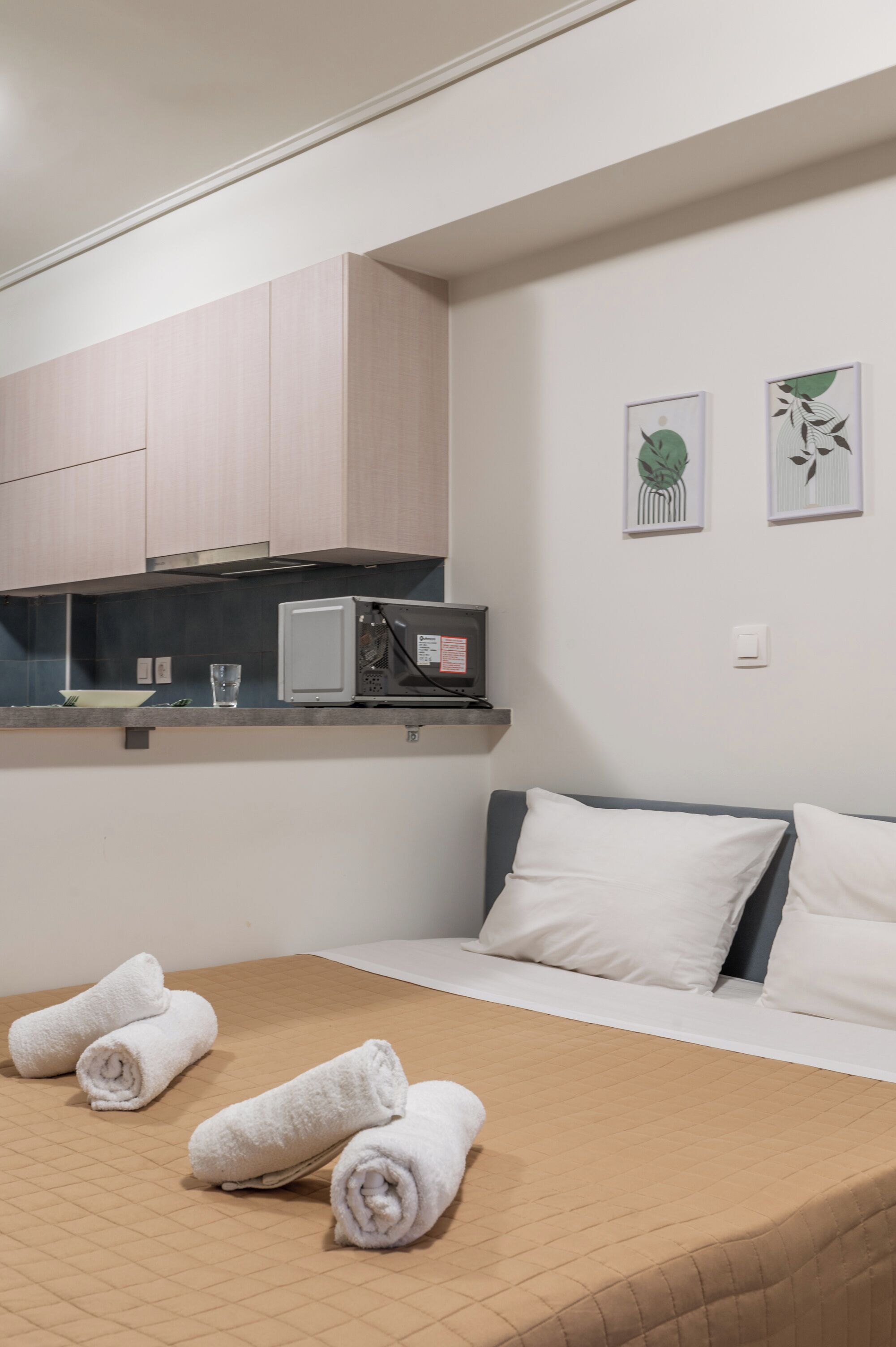 A hotel room with a bed, pillows, a TV, a microwave, and towels on the bed.