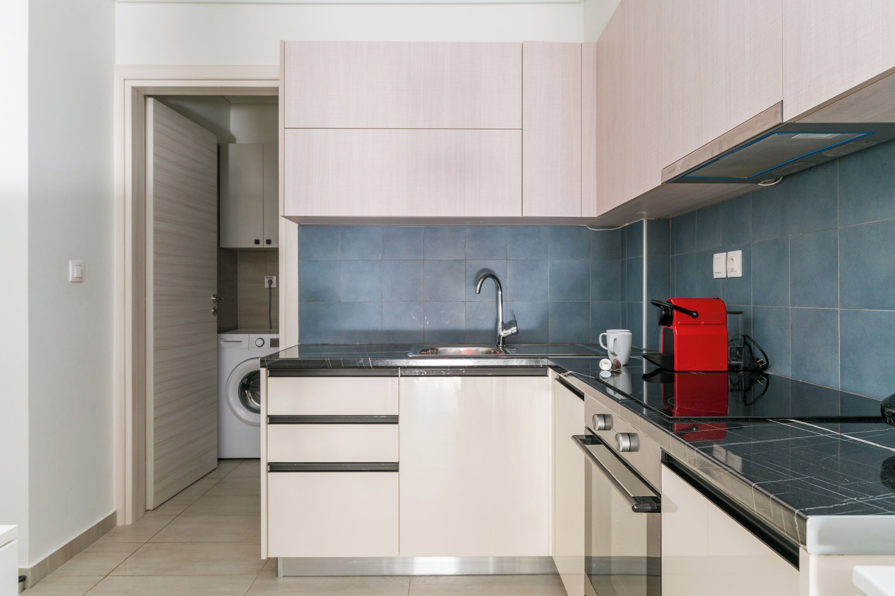 A compact kitchen with a washing machine, a coffee machine, and a sink.