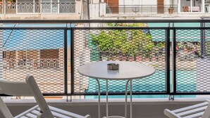 A balcony with two white chairs and a small round table, overlooking a courtyard with a pool and buildings in the background. - Elvita Apartments 4 Athens (ATHINA)