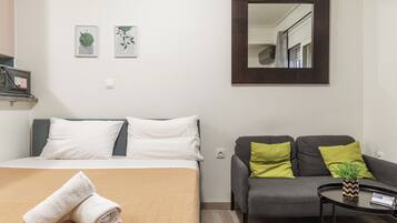 Habitación de hotel con cama, sofá, una pequeña mesa con una planta y dos cuadros en la pared.