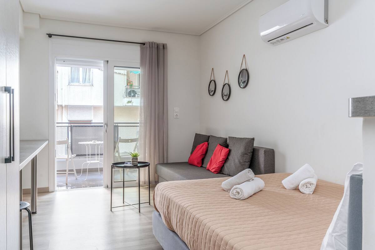 Una habitación de hotel moderna con una cama, una mesita pequeña, un sofá y un balcón con vistas.