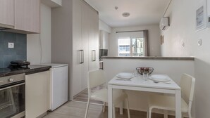 A compact kitchen with a dining area, white cabinetry, a small refrigerator, and a window with a view. - Elvita Apartments 4 Athens (ATHINA)