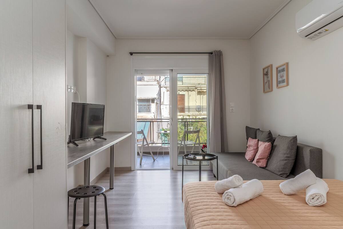 Una habitación de hotel moderna con cama, televisión, balcón con vistas y una pequeña mesa con toallas.