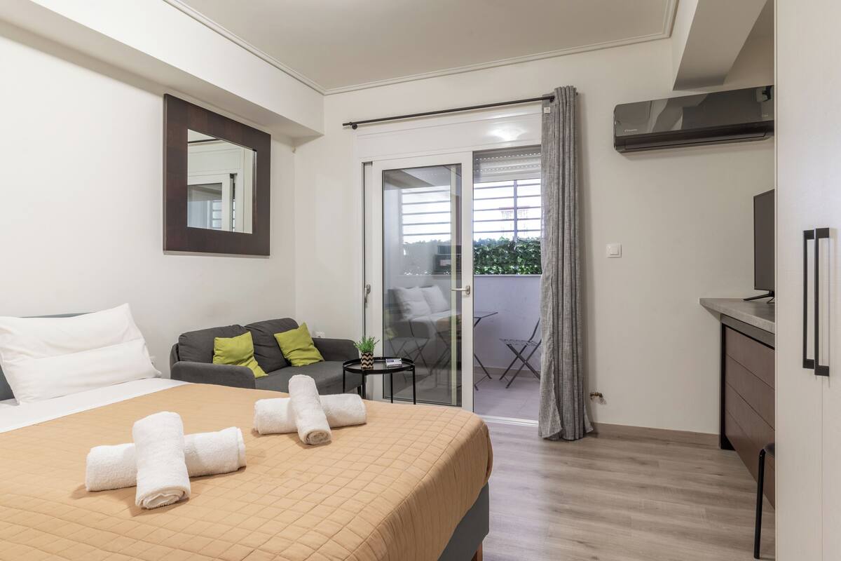 Habitación de hotel con cama, sofá, una mesita con planta, balcón y televisión.