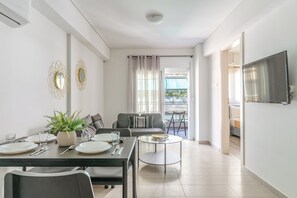 Una sala de estar moderna con comedor, sofá, televisor y balcón con cortinas.