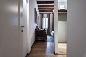 Ein Flur mit Holzboden, einem Bett mit Kopfteil, einem Schminktisch und einem Fenster mit Vorhängen.